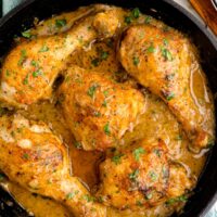 铸铁煎锅放在茶巾上。煎锅中有五块肉汁中的鸡肉鸡。